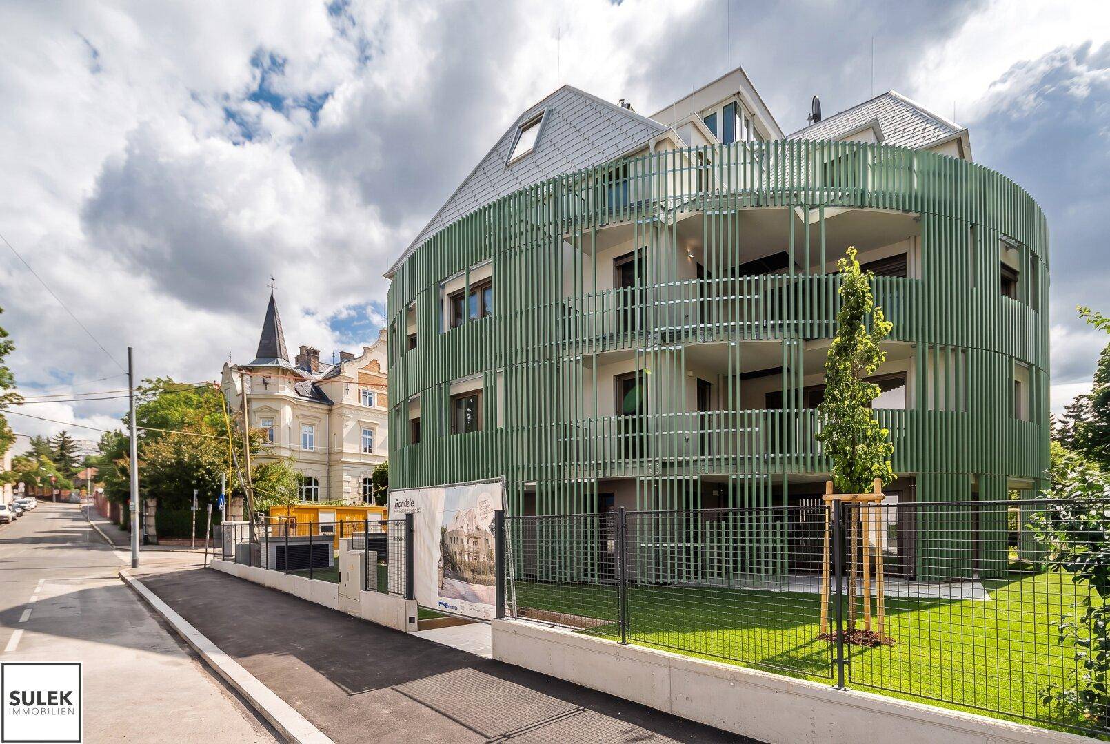 Elegantes, modernes Gebäude mit markanter grüner Fassade und Balkonen an einer ruhigen Straße.