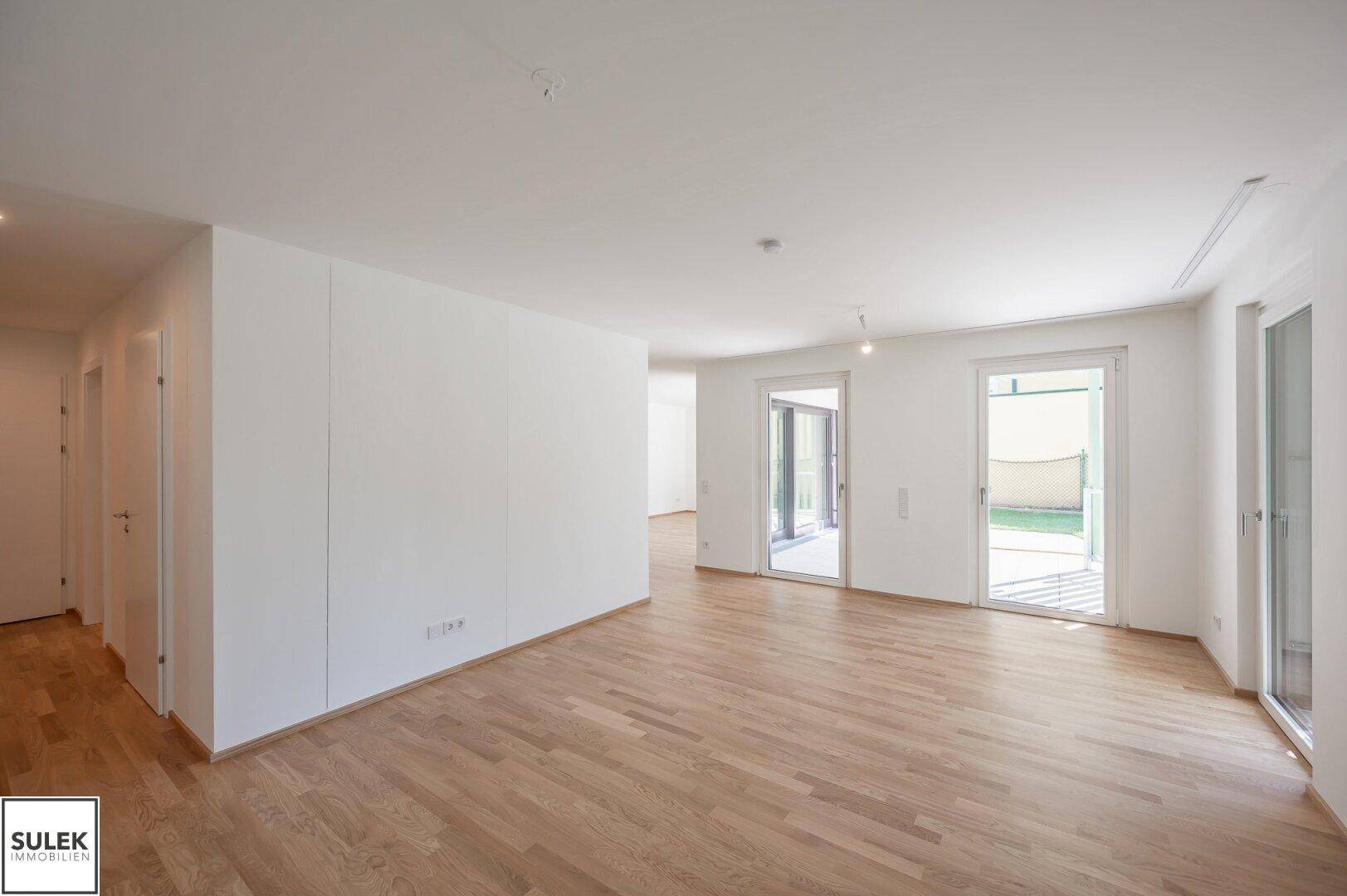 Geräumiger, heller Raum mit Parkettboden und mehreren Fenstertüren zum Außenbereich.