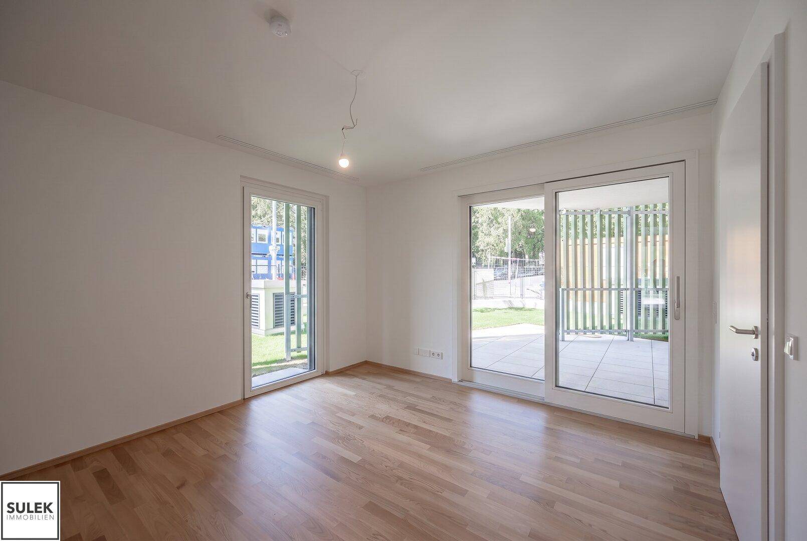 Helles Schlafzimmer mit Parkettboden und großem Schiebefenster zum Außenbereich.