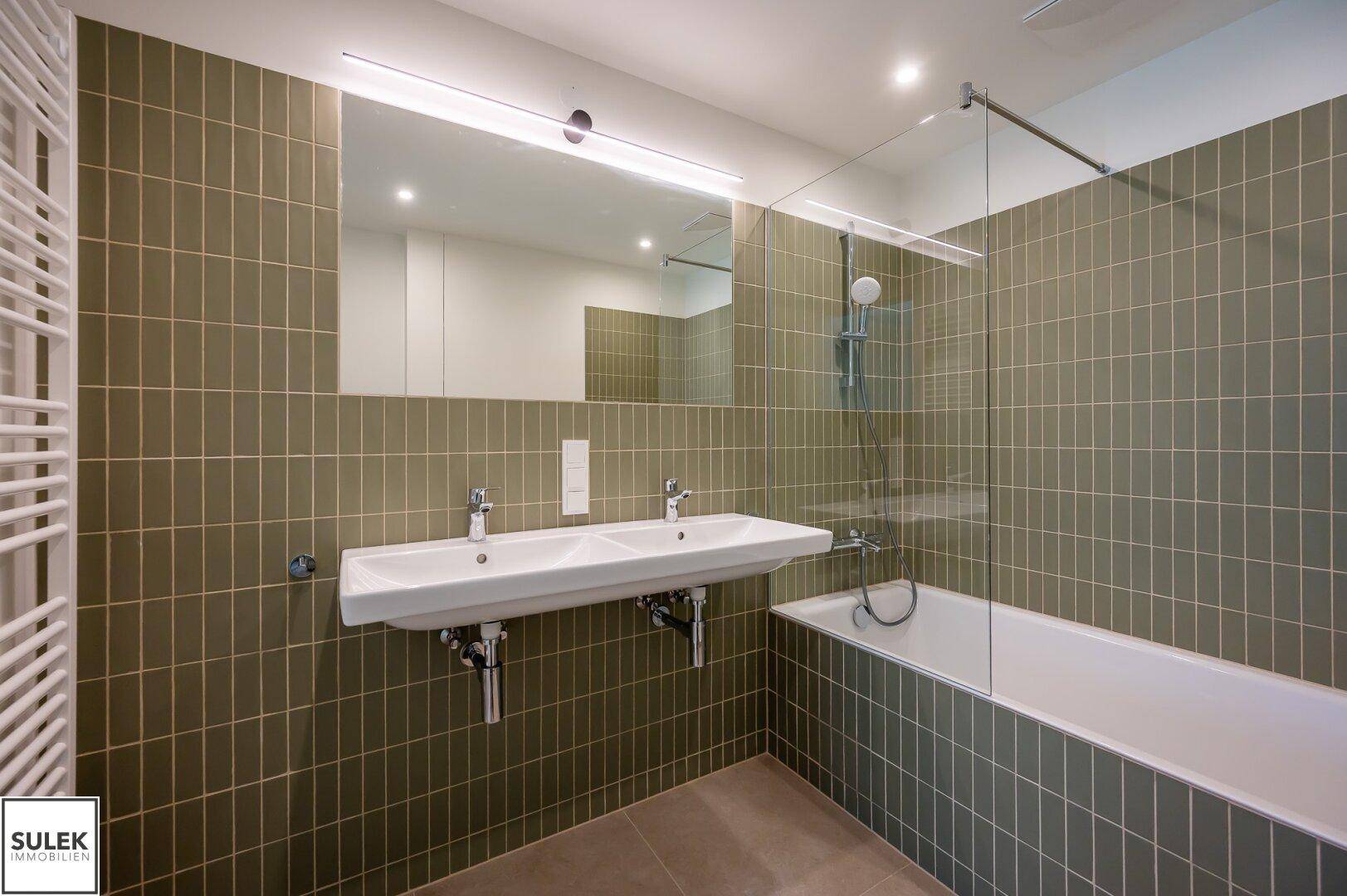Modernes Badezimmer mit doppelter Waschtischplatte, Badewanne und olivgrünen Fliesen.