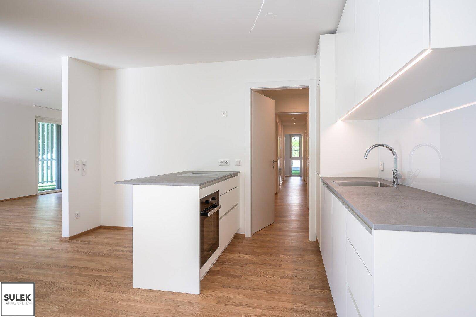Moderne Einbauküche mit Kochinsel und hellem Parkettboden, offen zum Flur.
