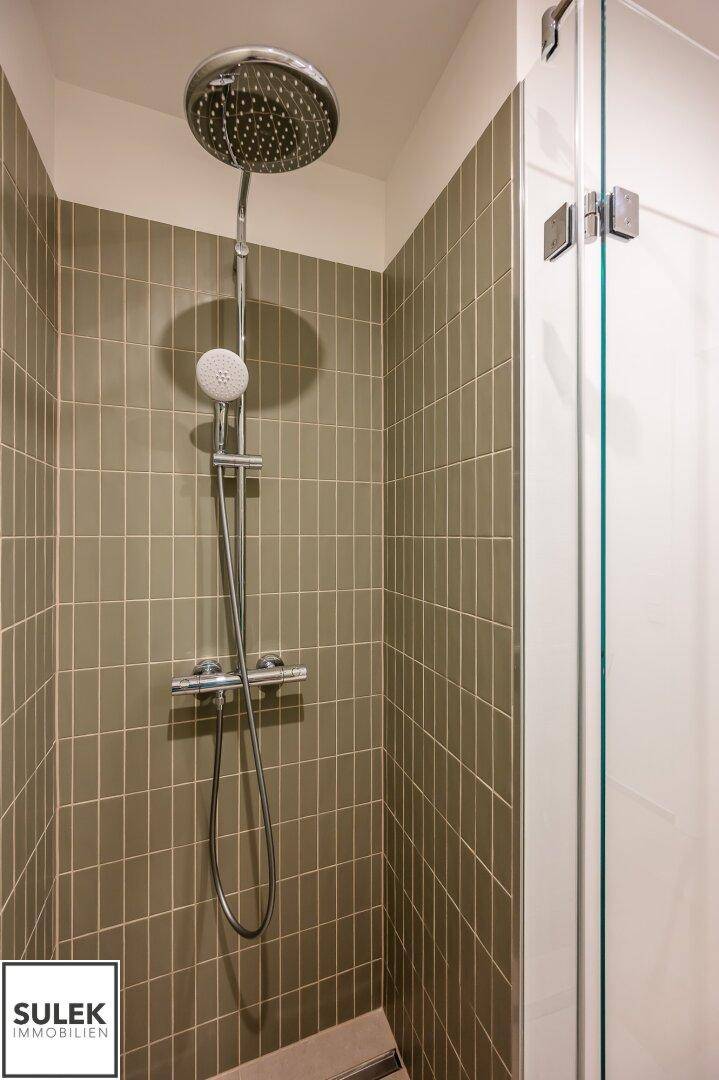 Detailaufnahme einer modernen Regendusche in einem gefliesten Duschbereich.