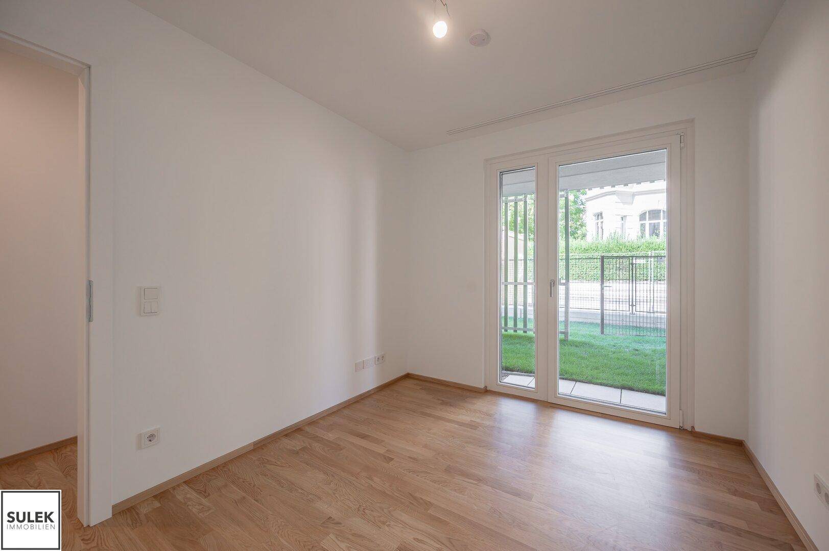 Helles Zimmer mit Parkettboden und Zugang zu einem kleinen Außenbereich mit Rasen.