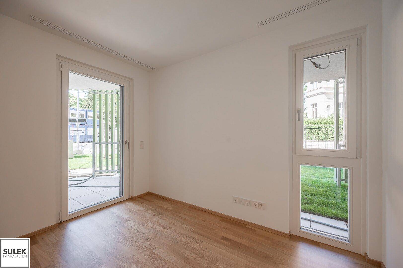 Geräumiges Zimmer mit Parkettboden und großen Fenstern, die viel Licht spenden.