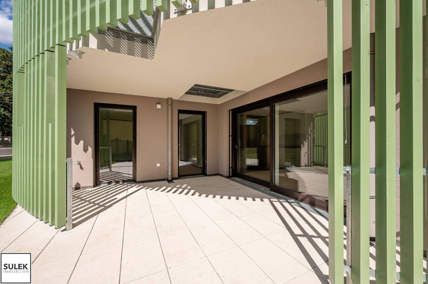 Moderne Terrasse mit großen Glasschiebetüren und grünen vertikalen Lamellen als Sichtschutz.