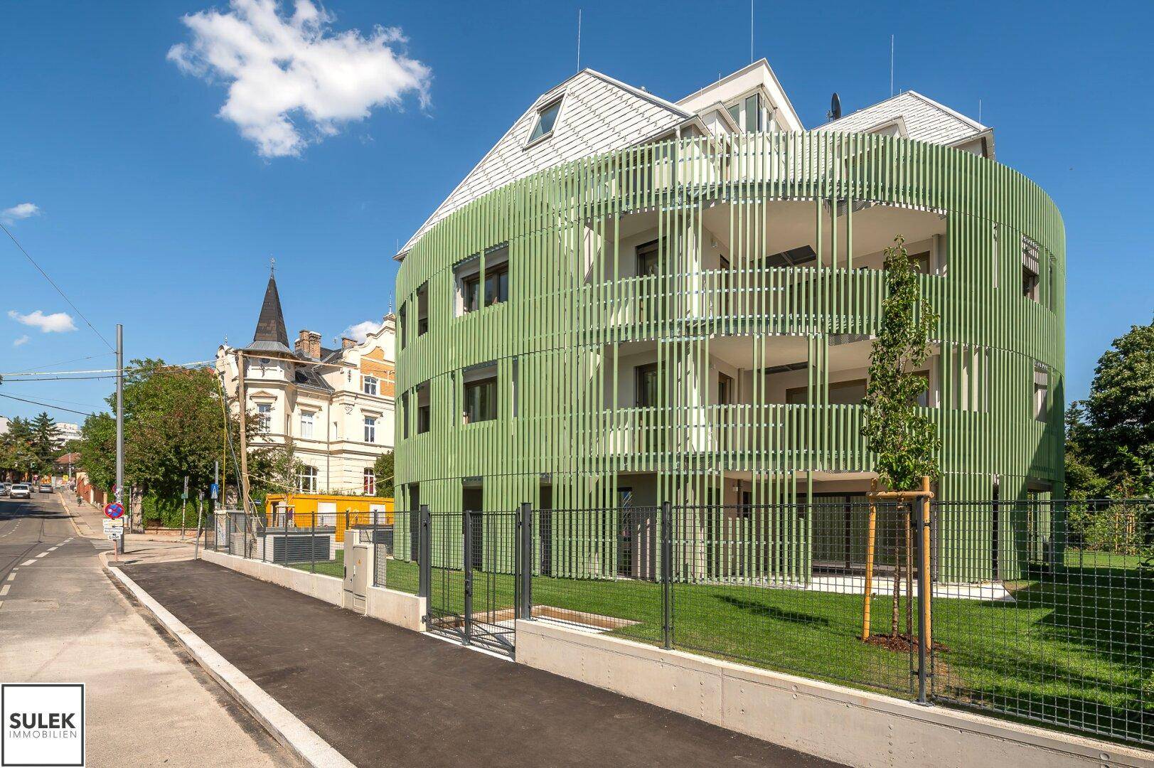 Modernes Wohngebäude mit markanter grüner Fassade und Zugang von der Straße.