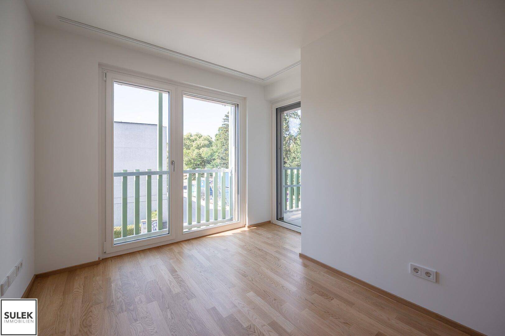 Schlafzimmer mit Parkettboden und direktem Zugang zum Balkon, hell und modern gestaltet.