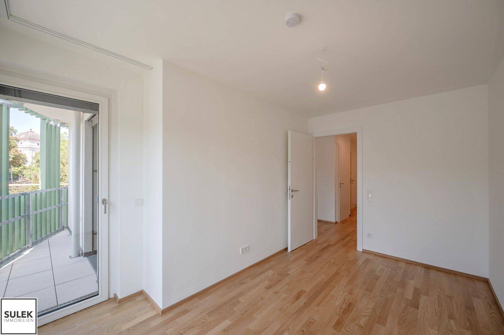 Geräumiges Zimmer mit Parkettboden und Balkonzugang, ideal als Schlafzimmer oder Büro.