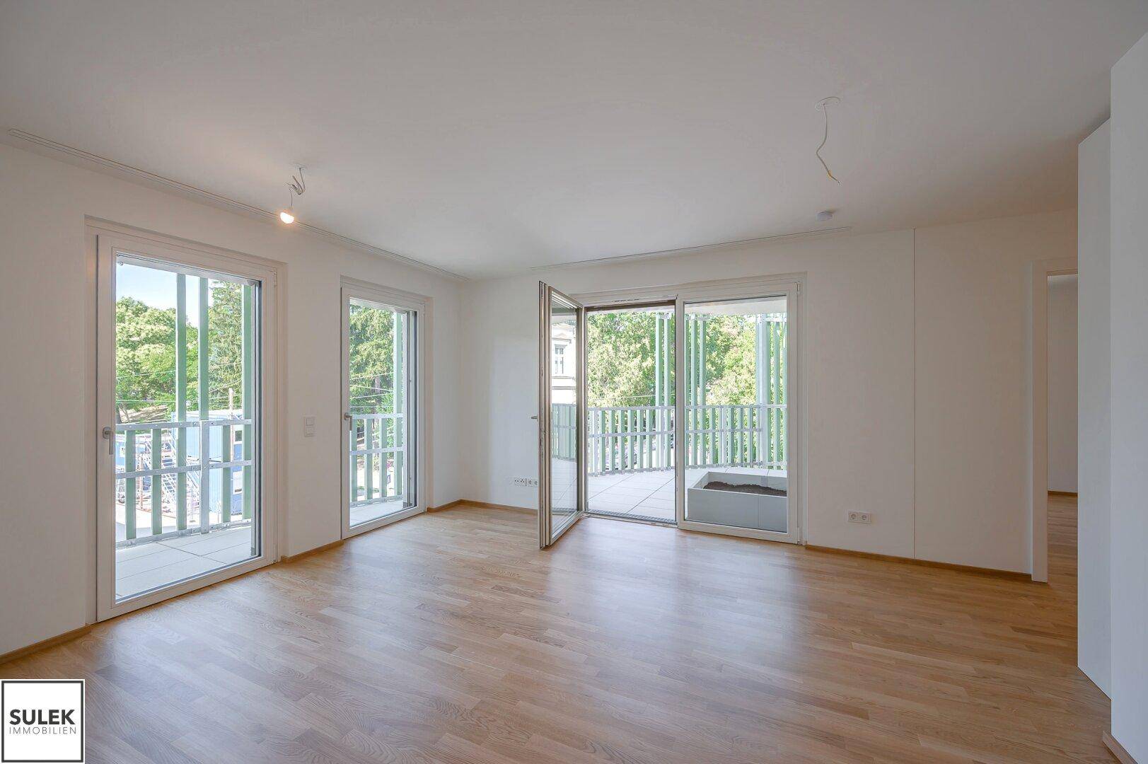 Großzügiger Wohnbereich mit Parkettboden und mehreren Fenstertüren zum Balkon, sehr hell.