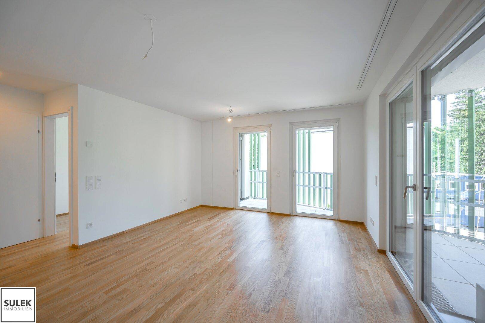 Lichtdurchfluteter Raum mit Parkettboden und breiter Fensterfront zum Außenbereich, modern und offen.