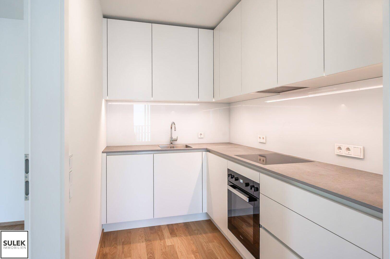 Moderne Einbauküche mit weißen Hochglanzfronten, Induktionskochfeld und Backofen, neuwertig und funktional.