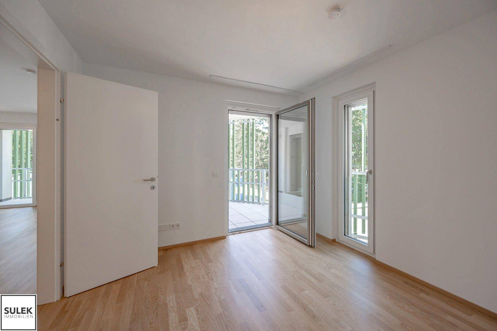 Helles Schlafzimmer mit Parkettboden und direktem Zugang zum Balkon, bereit zum Einzug.