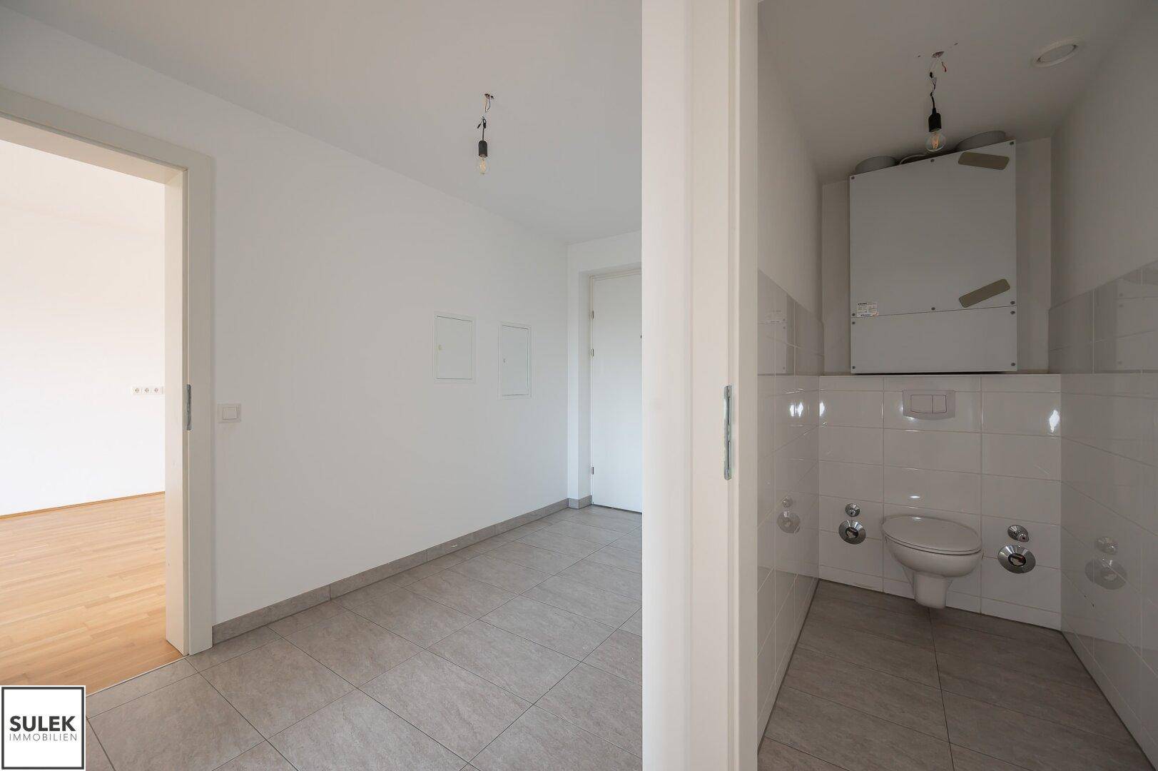 Kleines Gäste-WC mit weißen Fliesen und einfacher Toilette, angrenzend an einen Flur.