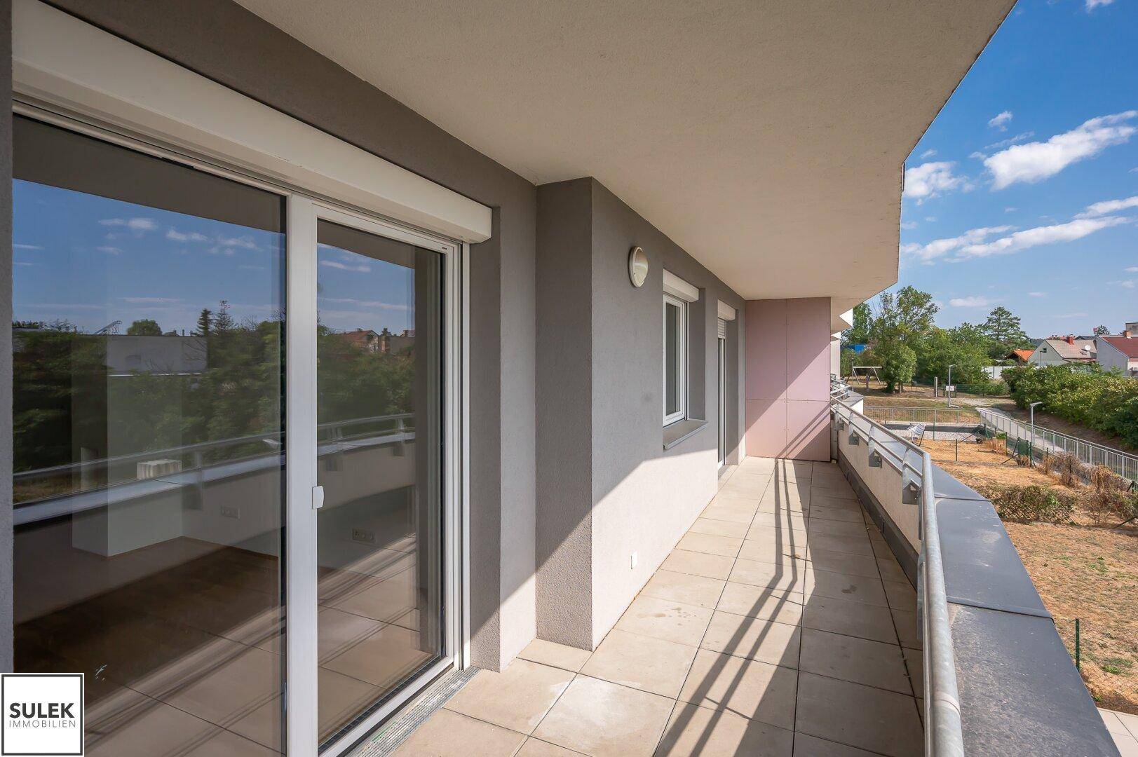 Geräumiger Balkon mit Schiebetür und Rollladen, bietet Zugang zu einem hellen Innenraum.