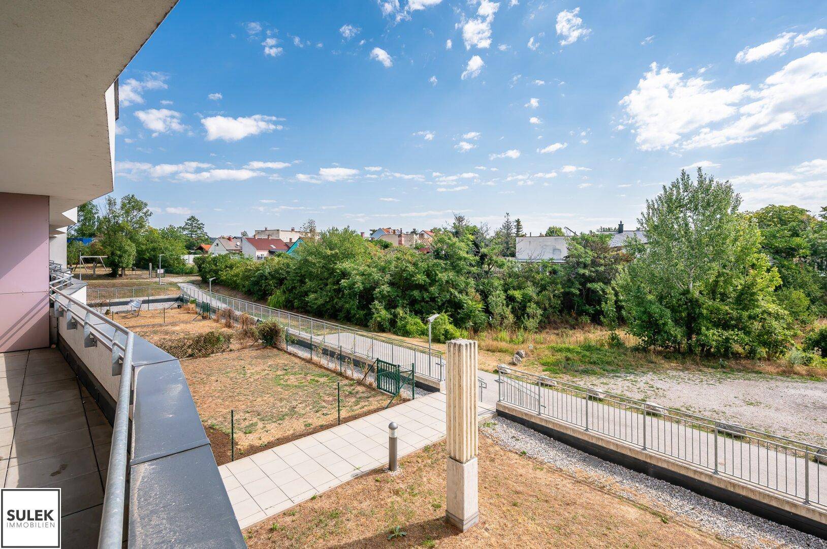 Weitläufiger Blick vom Balkon auf eine grüne Landschaft mit Bäumen und Wohngebäuden.