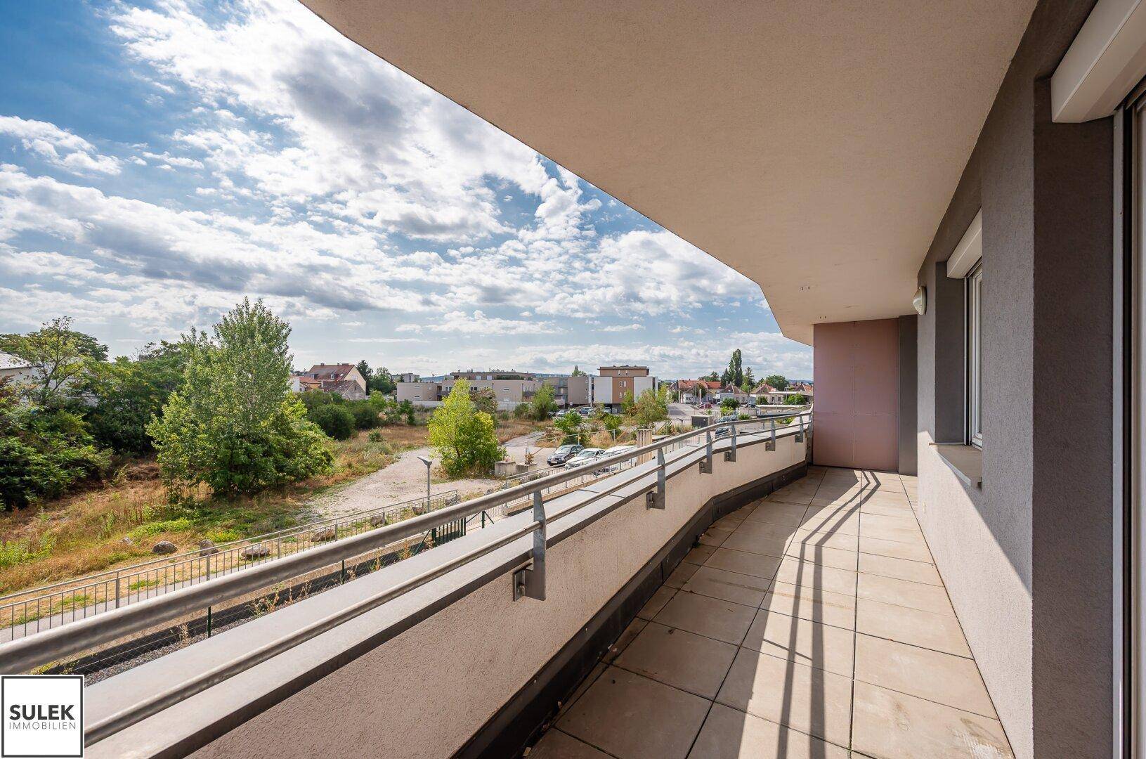 Langer Balkon mit Metallgeländer und weitem Blick ins Grüne und auf die Umgebung.
