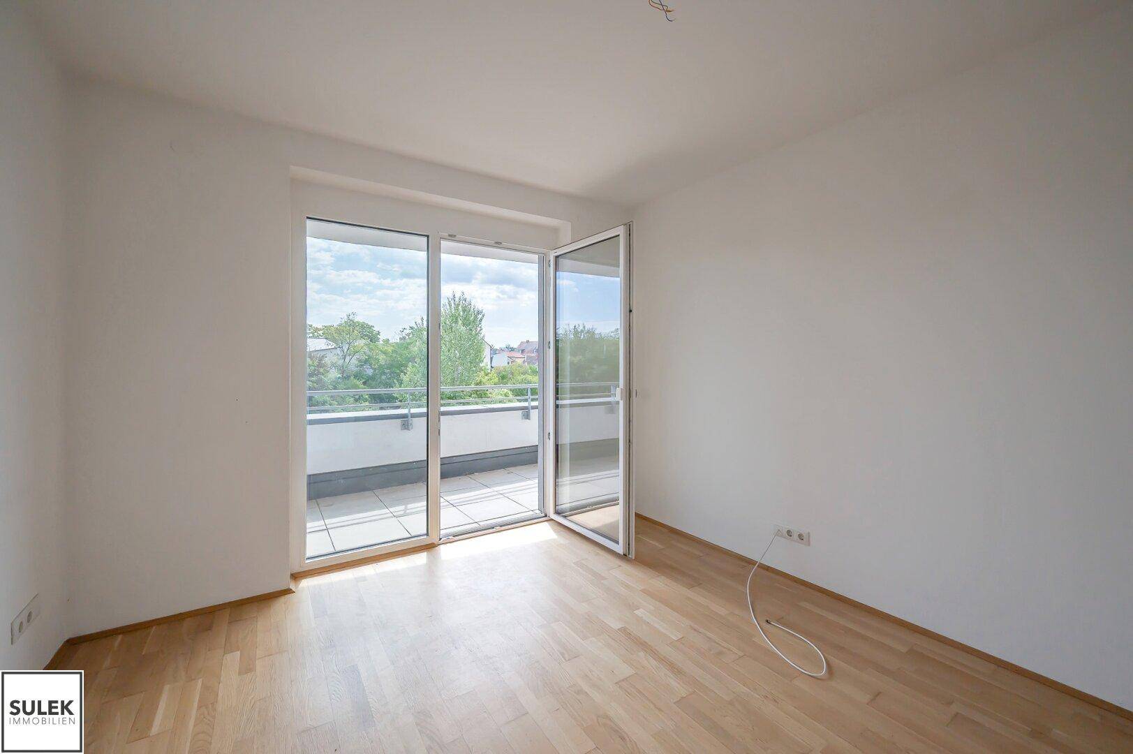 Heller Raum mit Parkettboden und großem Zugang zu einem sonnigen Balkon.