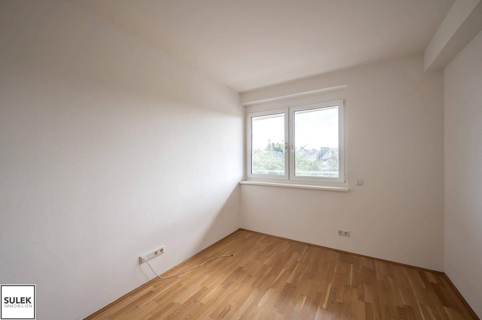 Schlafzimmer mit Parkettboden und einem Fenster, das viel Tageslicht hereinlässt.
