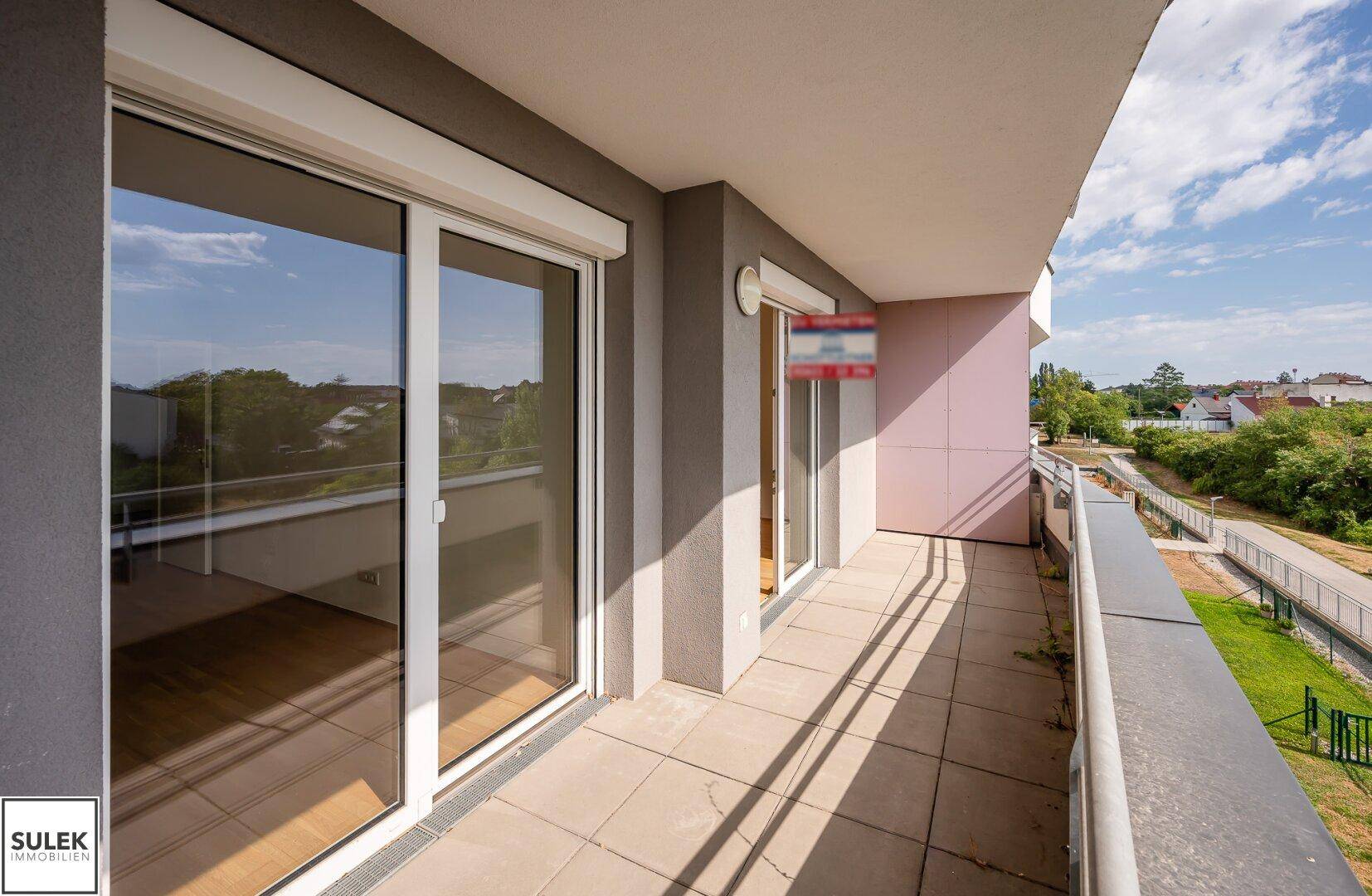 Langer Balkon mit Fliesenboden und Schiebetüren, der einen Blick auf die Umgebung bietet.