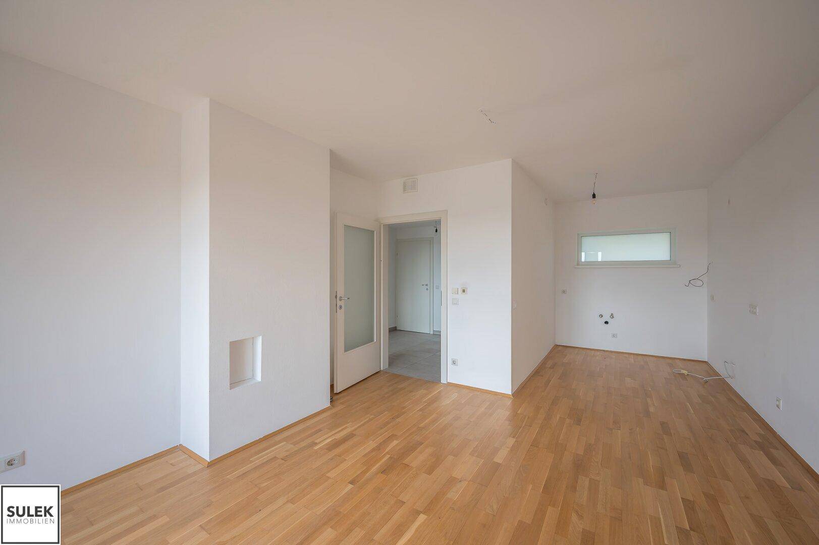 Geräumiges, leeres Zimmer mit Parkettboden und weiß gestrichenen Wänden, ideal für einen Wohnbereich.
