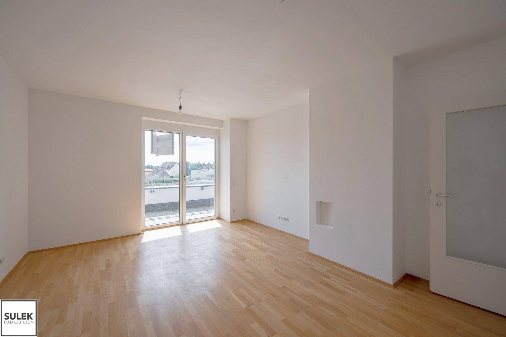 Helles, leeres Wohnzimmer mit Parkettboden und Zugang zu einem Balkon, bereit zur Einrichtung.