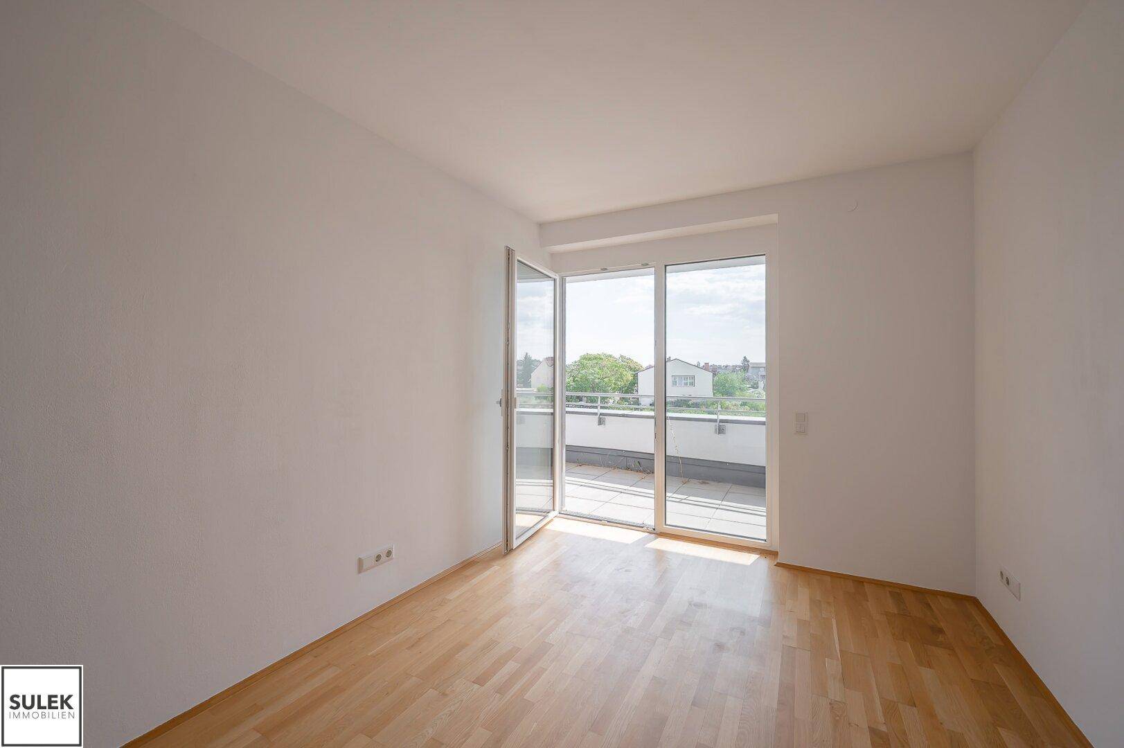 Helles Schlafzimmer mit Parkettboden und großen Fenstern, die Zugang zu einem Balkon bieten.