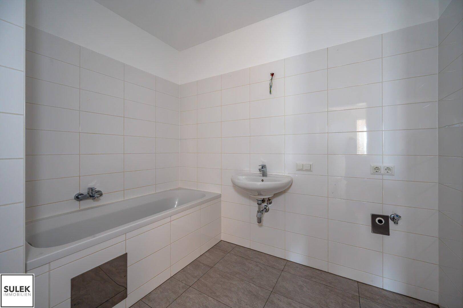 Helles Badezimmer mit Badewanne und Waschbecken, vollständig mit weißen Fliesen ausgestattet.