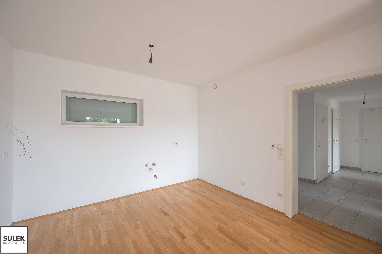 Leerer Küchenbereich mit Parkettboden und Fenster, bereit für die Installation einer Einbauküche.