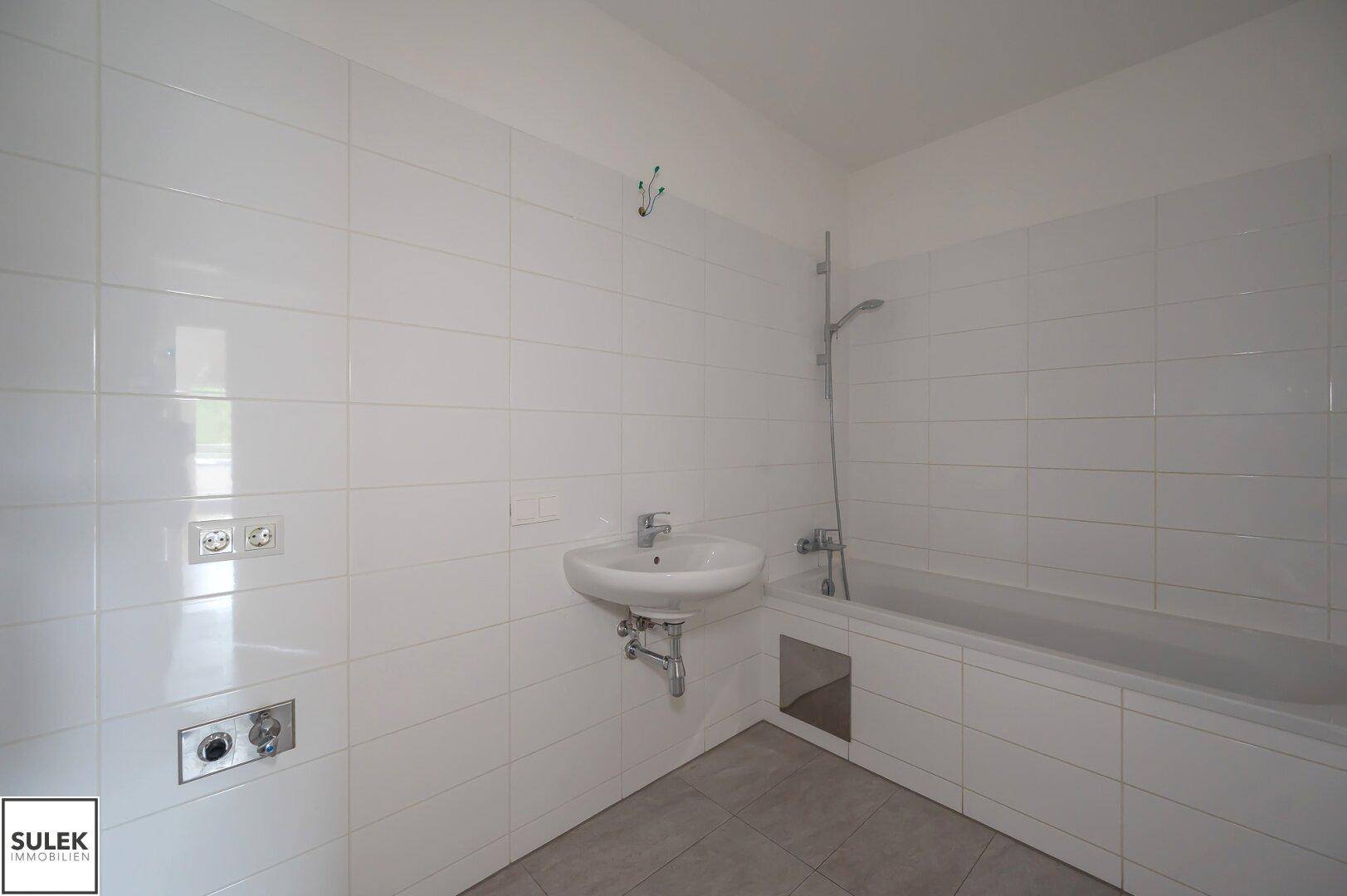 Modern gefliestes Badezimmer mit Waschbecken und Badewanne, in hellen Farben gehalten.