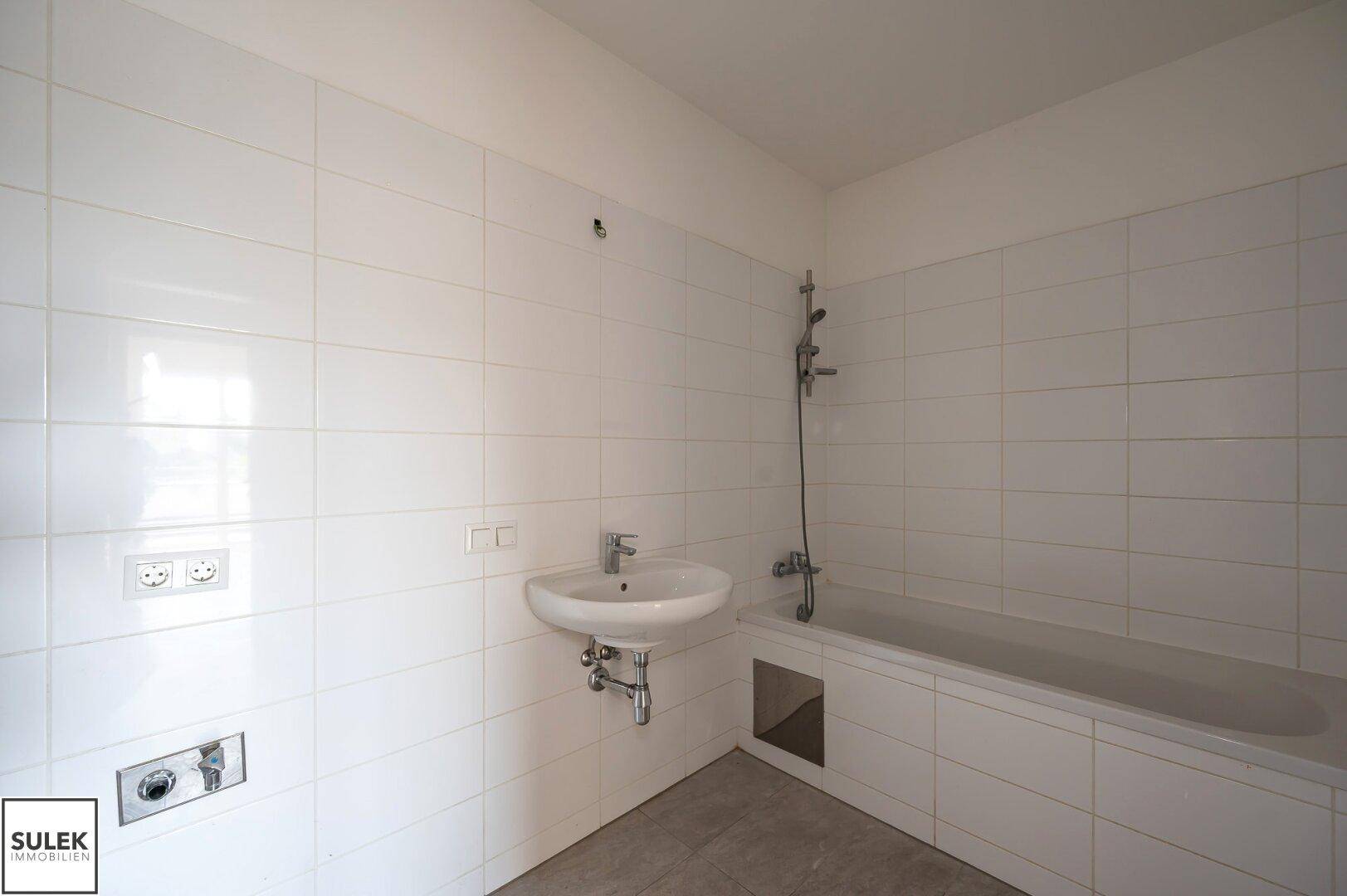 Badezimmer mit Badewanne, Waschbecken und weißen Fliesen, bereit für die Fertigstellung.