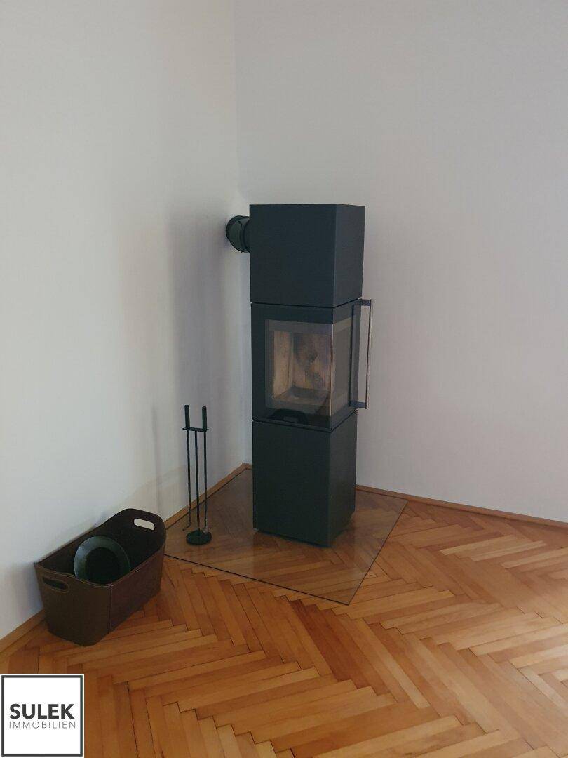 Moderner Kaminofen in der Ecke eines Raumes mit hellem Fischgrätparkettboden und weiß gestrichenen Wänden.