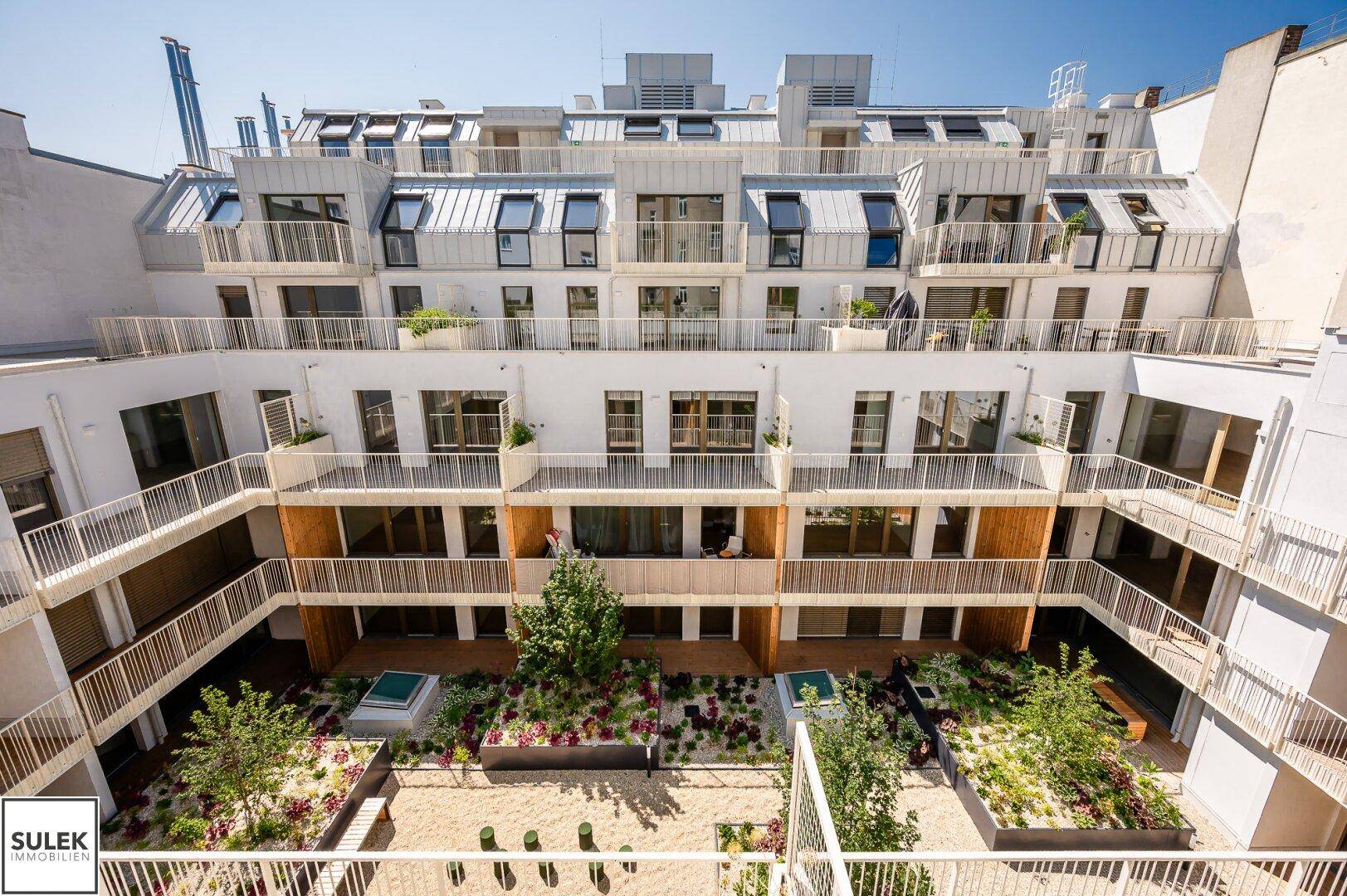 Innenhof eines modernen Wohnkomplexes mit mehreren Balkonen und einer begrünten Gartenanlage.