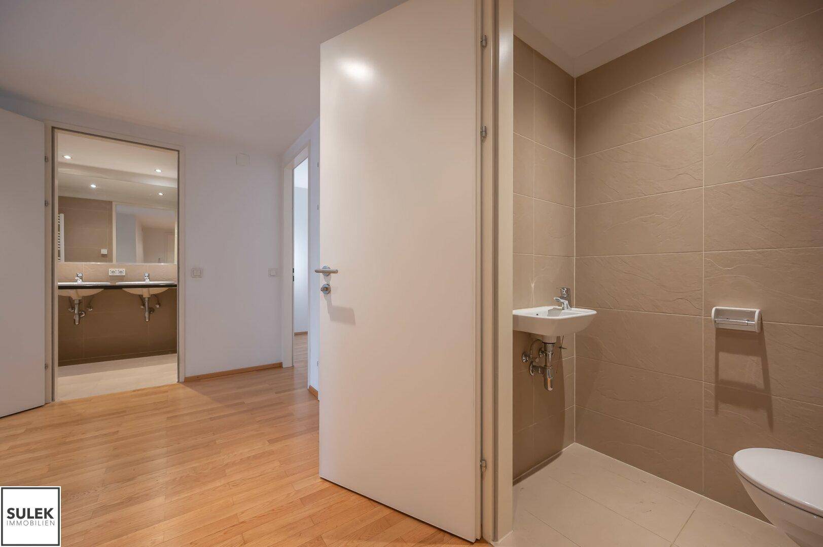 Flur mit Zugang zu einem Gäste-WC und einem Badezimmer mit Doppelwaschbecken.