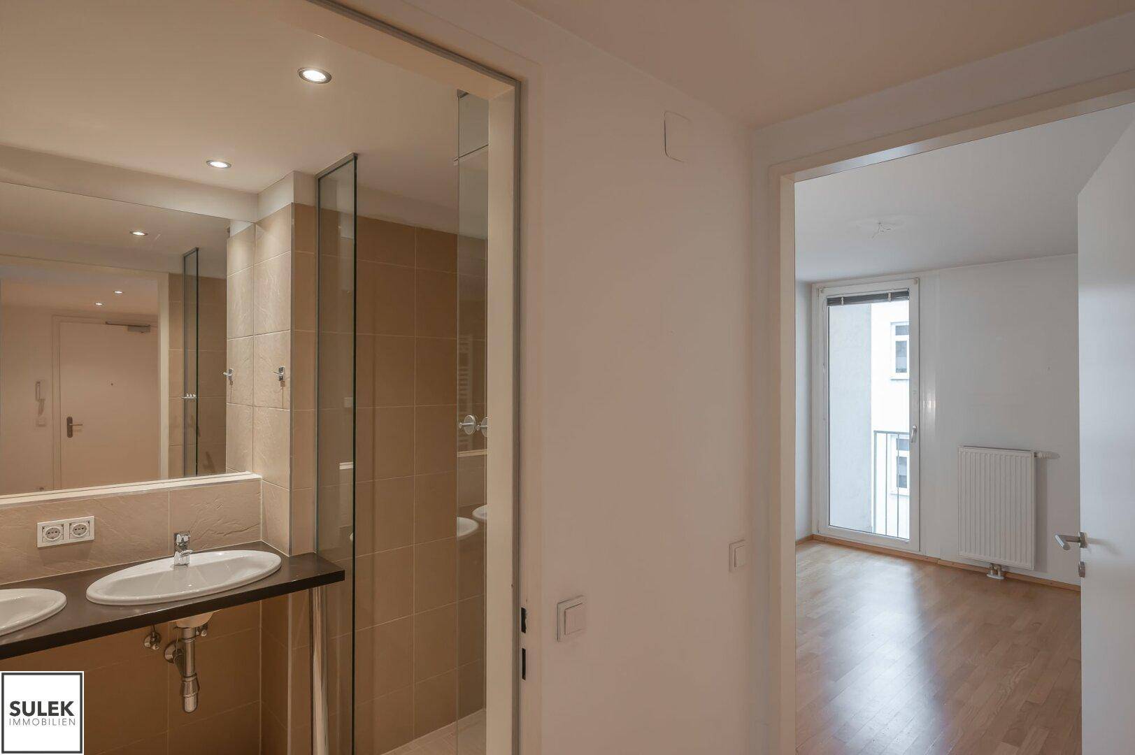 Heller Flur mit Zugang zu einem modernen Badezimmer mit Dusche und einem Zimmer mit Balkon.