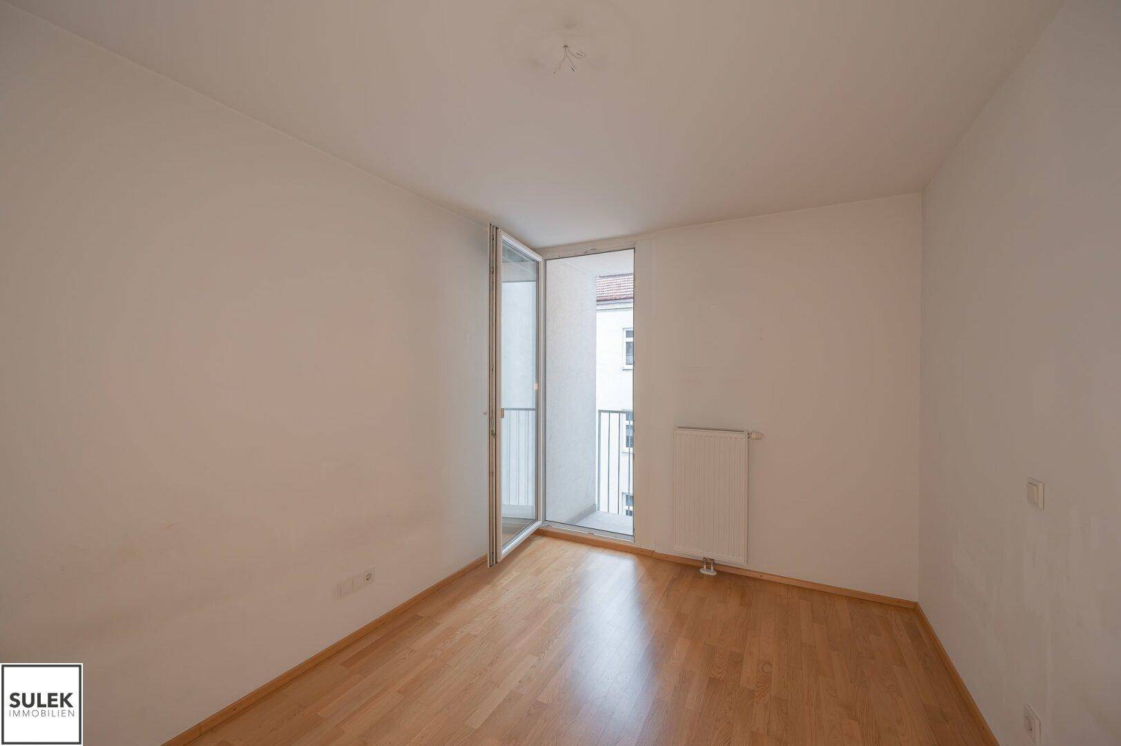 Leeres Zimmer mit Holzfußboden und Zugang zu einem französischen Balkon.