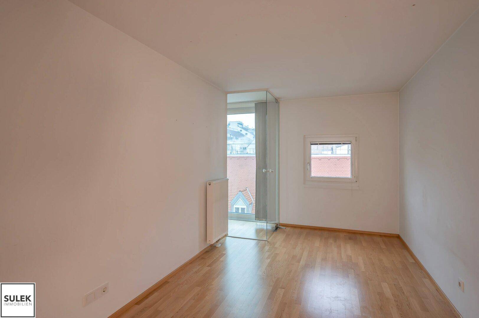 Helles Zimmer mit großen Fenstern, Schiebetür und Glasabtrennung, bietet viel Tageslicht.