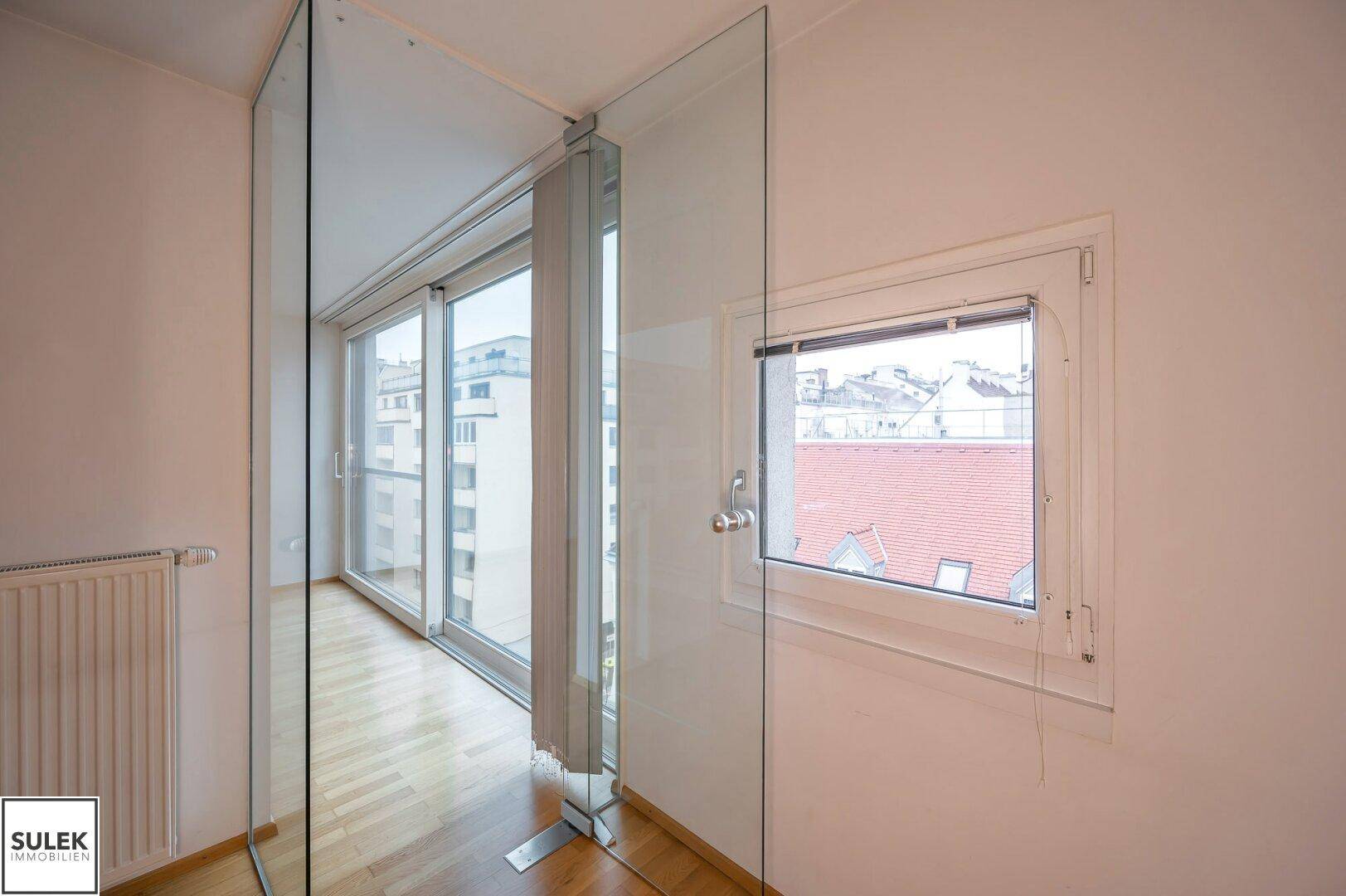 Helles Zimmer mit großen Fenstern, Schiebetür und Glasabtrennung, bietet viel Tageslicht.