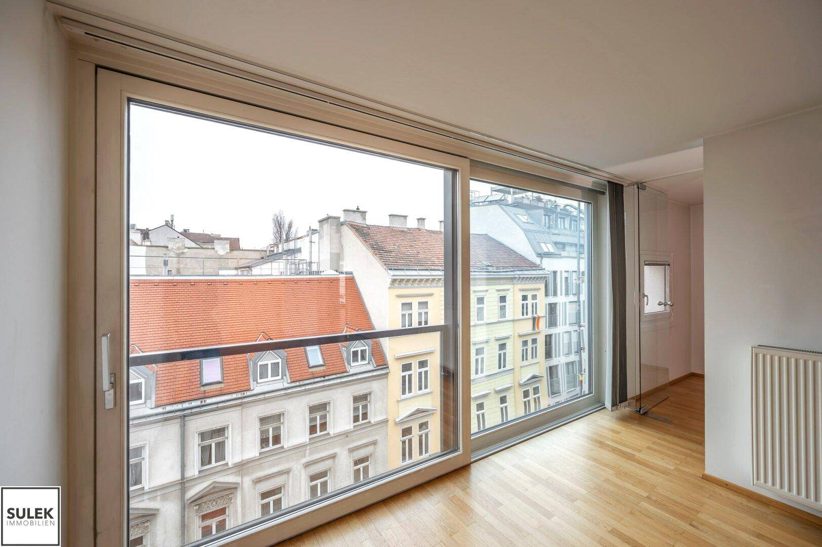 Heller Wohnraum mit großen Schiebetüren und Blick auf die umliegenden Stadtgebäude.