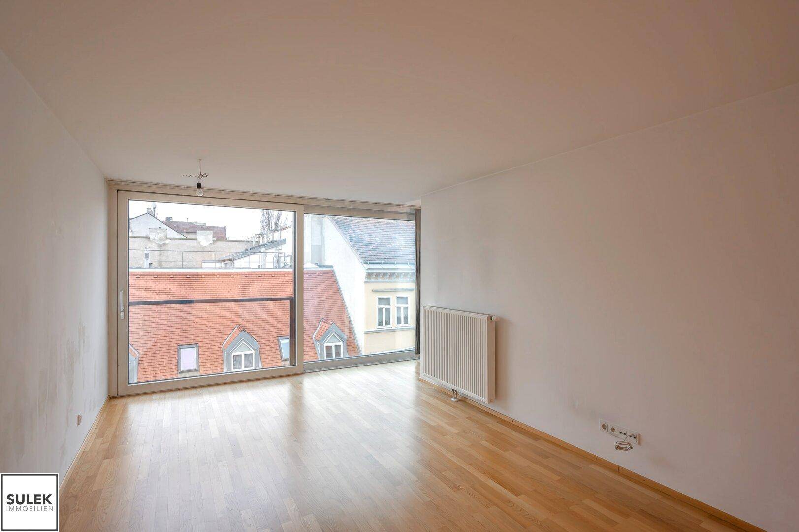Geräumiger Wohnraum mit breiter Fensterfront und Blick auf die Dächer der Stadt.