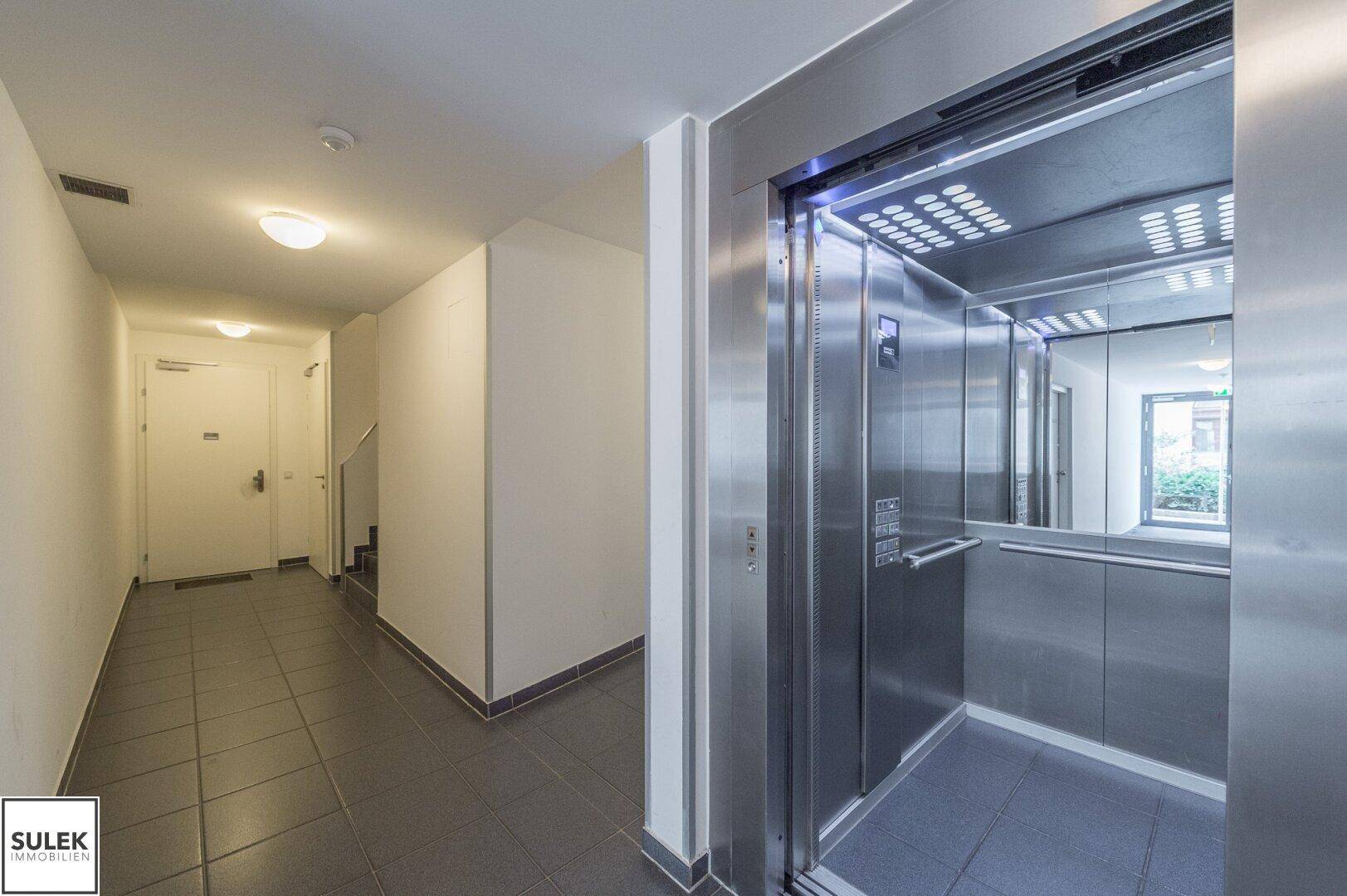 Heller Eingangsbereich mit modernem Aufzug und gefliestem Boden im Gemeinschaftsbereich.