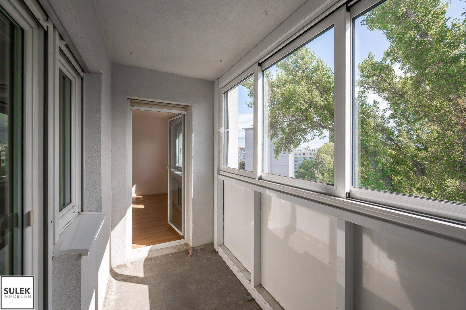 Verglaster Balkon mit Blick ins Grüne und viel Tageslicht, ideal zum Entspannen.