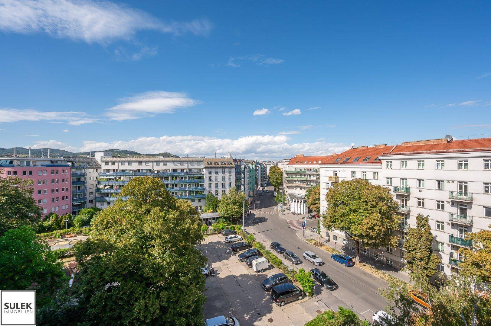Weitläufiger Blick auf eine städtische Wohngegend mit vielen Bäumen und Gebäuden unter blauem Himmel.