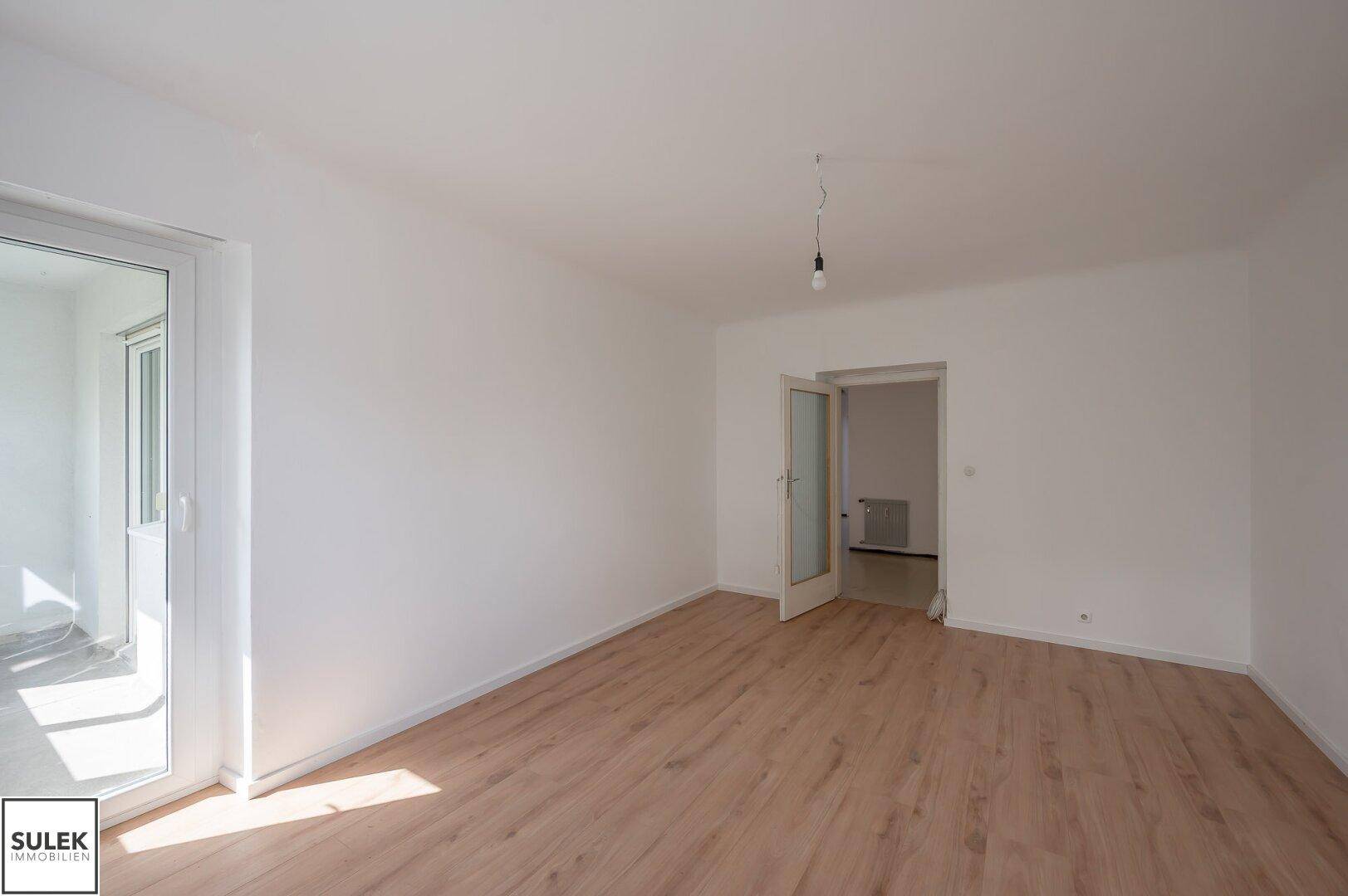 Helles Zimmer mit Laminatboden und Zugang zu einem sonnigen Balkon, bereit zur individuellen Gestaltung.