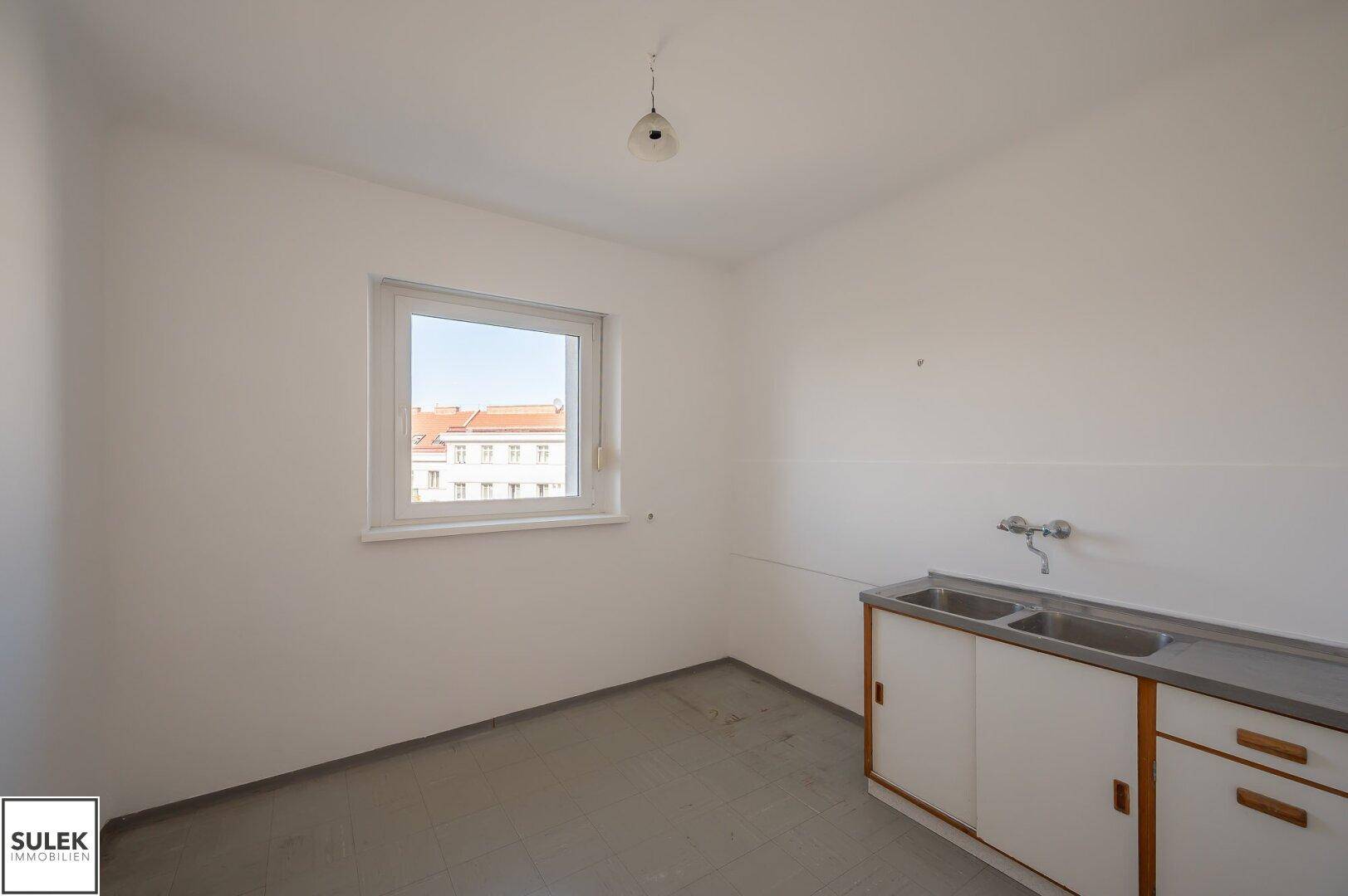Leere Küche mit Fenster, Spülbecken und Platz für eine individuelle Kücheneinrichtung.
