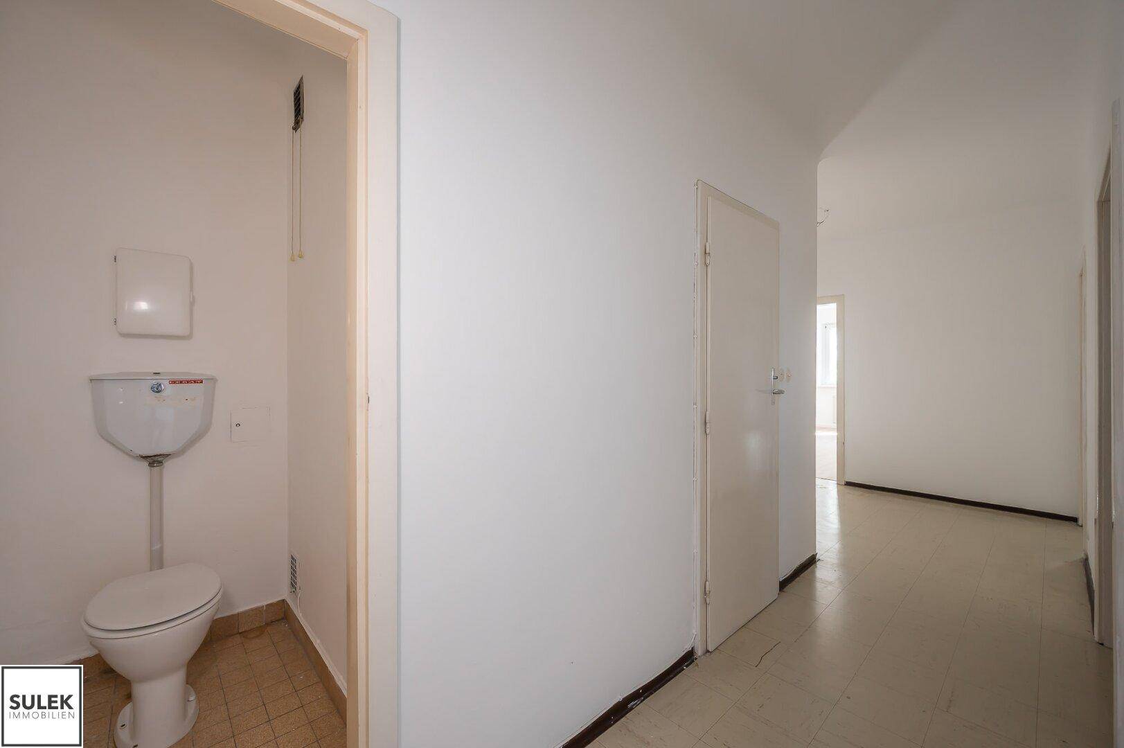 Flur mit Zugang zu einer separaten Toilette, ausgestattet mit einfachen Fliesen.