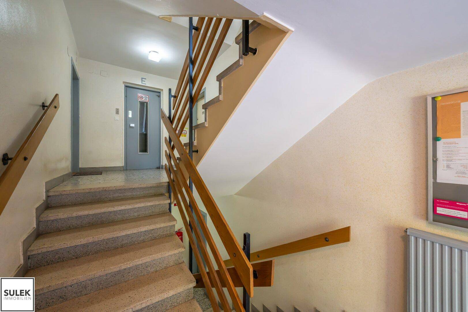 Treppenhaus mit Holzgeländer und Aufzug im Hintergrund, gut gepflegter Gemeinschaftsbereich.