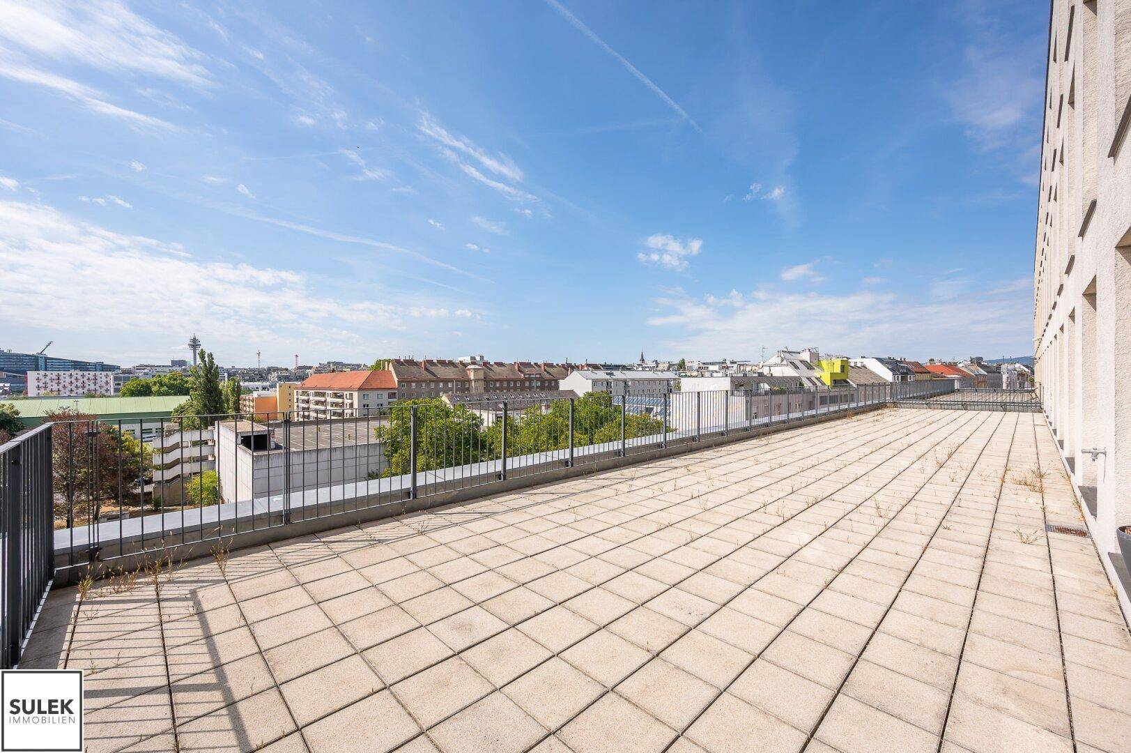 Große Dachterrasse mit Fliesenboden und weitem Blick über die Stadt und umliegende Gebäude.