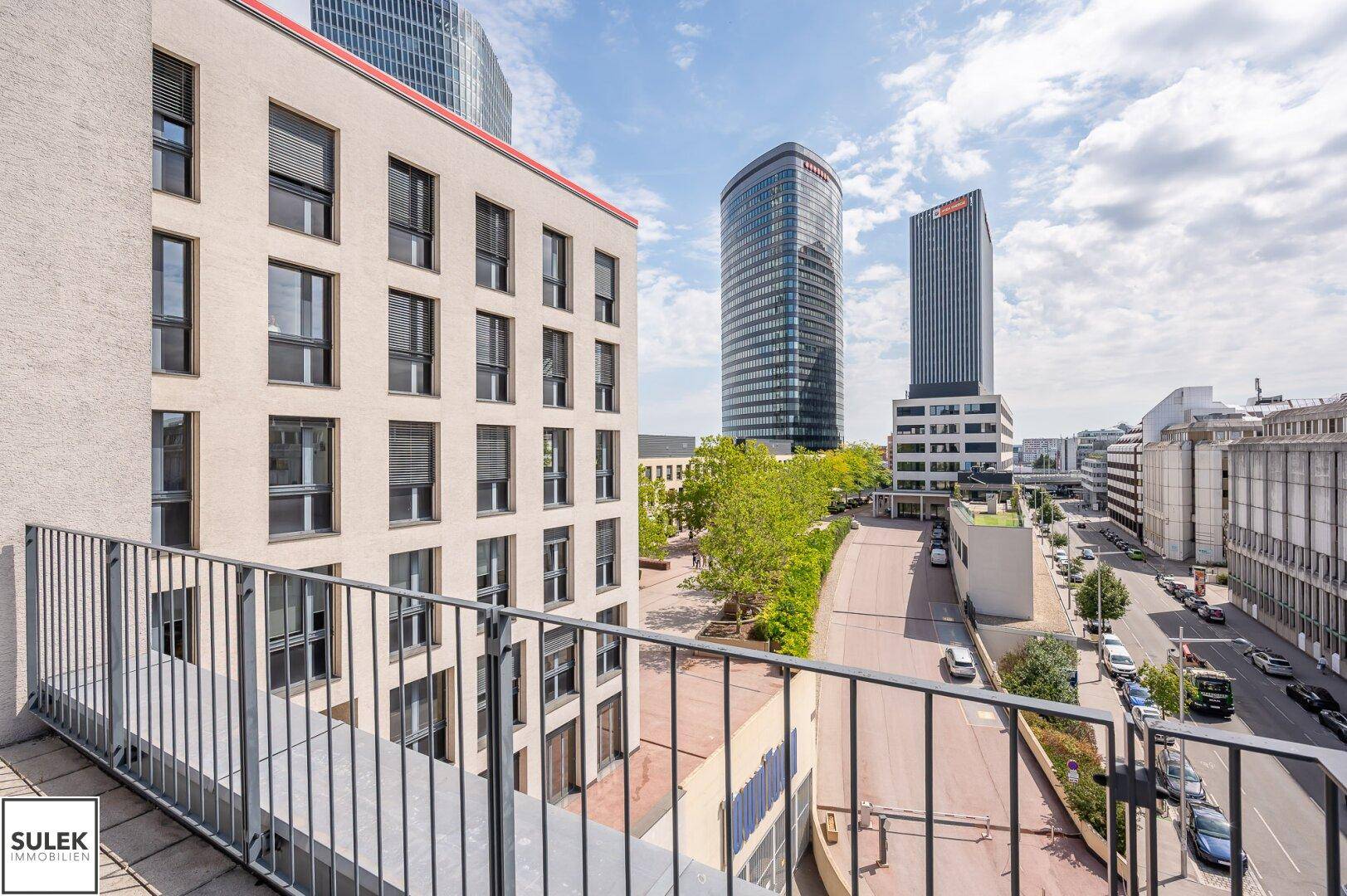Balkon mit Blick auf moderne Hochhäuser und die Stadtlandschaft unter blauem Himmel.