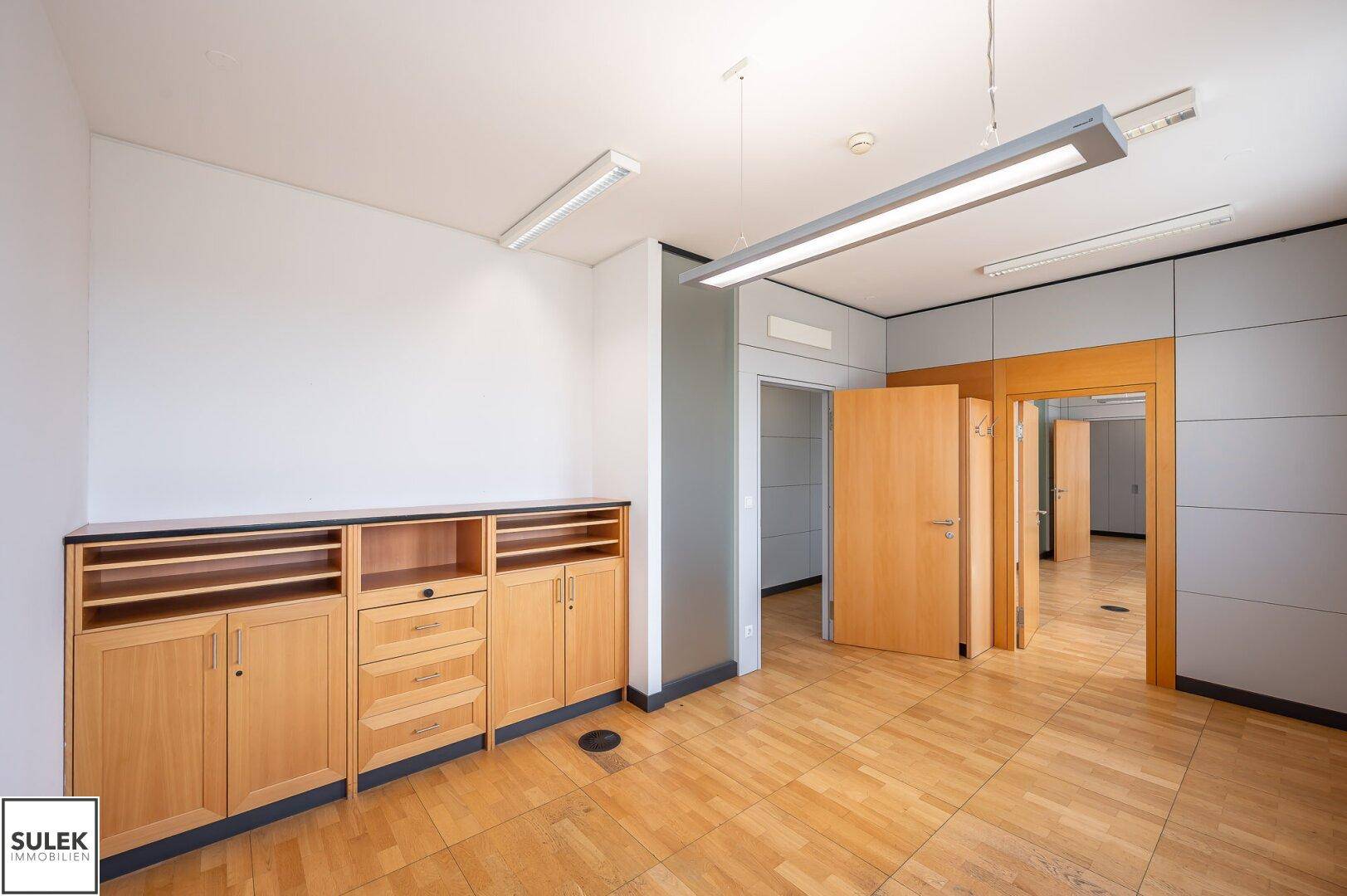 Büro mit Einbauschränken aus Holz, hellem Holzboden und weiß gestrichenen Wänden.
