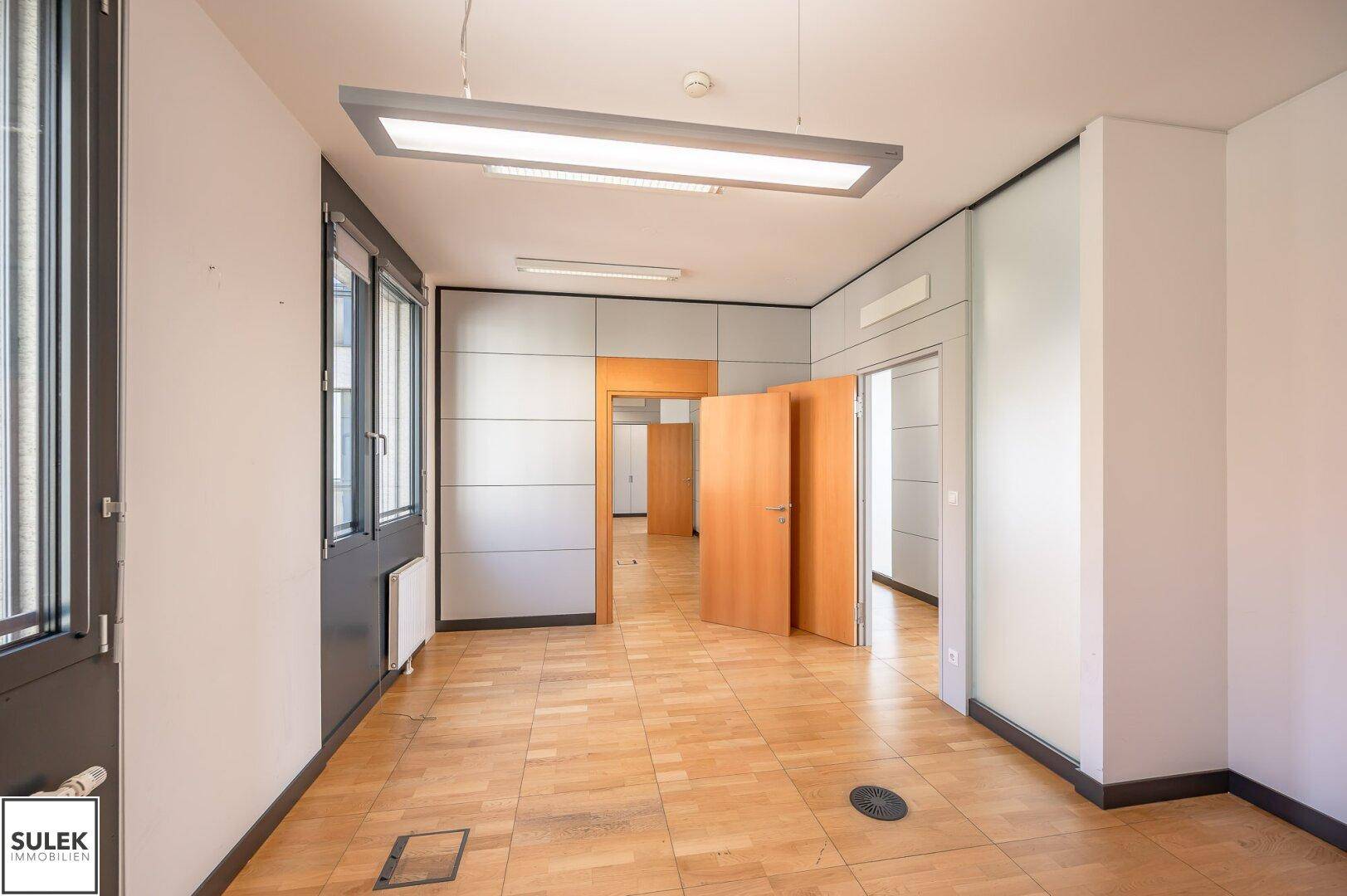 Geräumiges Büro mit Holzboden und Zugang zu weiteren Büroräumen durch offene Türen.